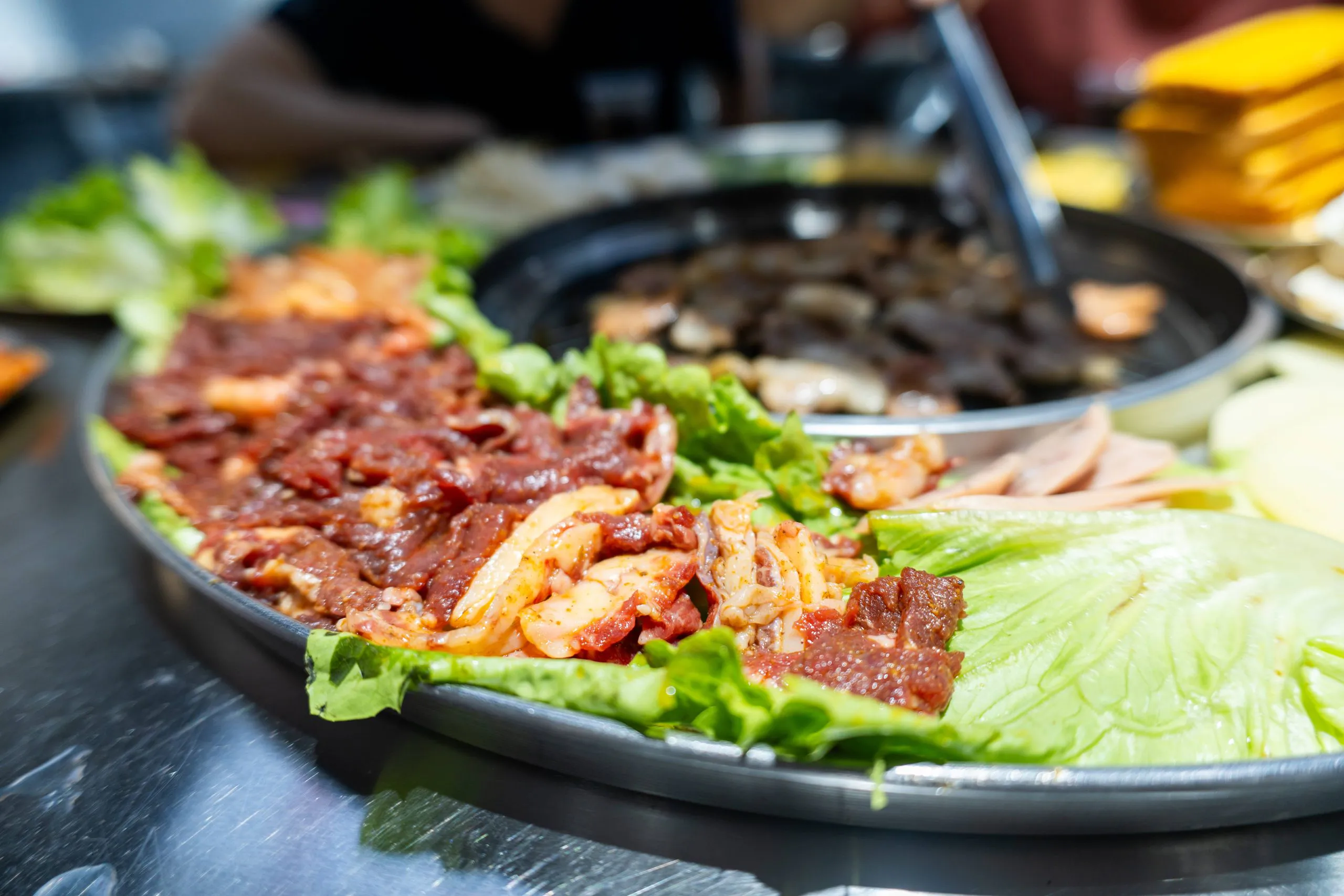 Marinated Korean BBQ meat with lettuce and vegetables beside a tabletop grill